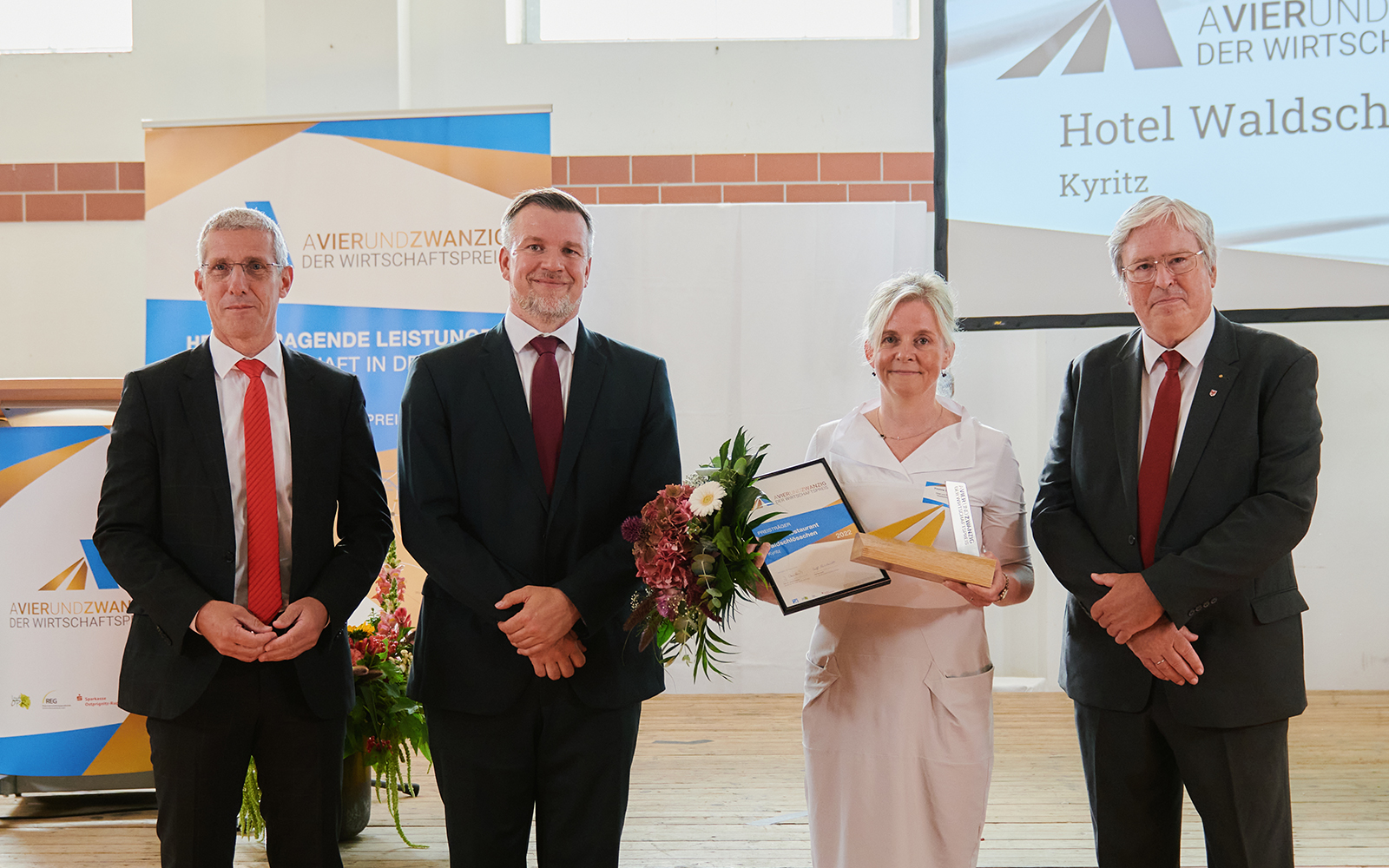 Das Foto zeigt vier Menschen, die nach der Preisverleihung des AVIERUNDZWANZIG Wirtschaftspreises 2022 in die Kamera schauen. Von links nach rechts: Markus Rück, Ralf Reinhardt Yvonne Schwarzer und rechts den damaligen Wirtschaftsminister Jörg Steinbach.